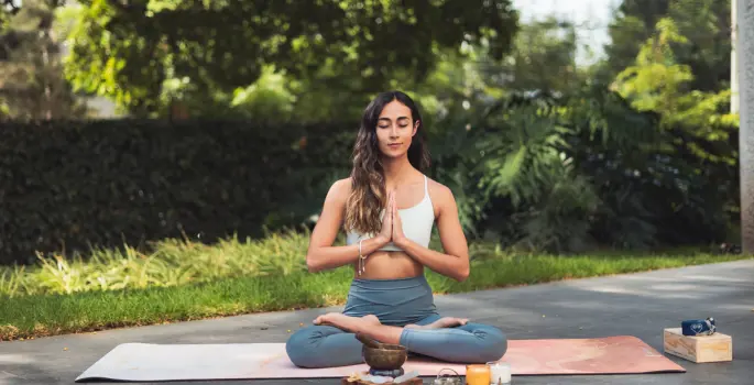 Woman sits outside on yoga mat in meditative pose
