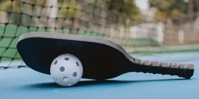 A pickleball and paddle are displayed on a pickleball court.