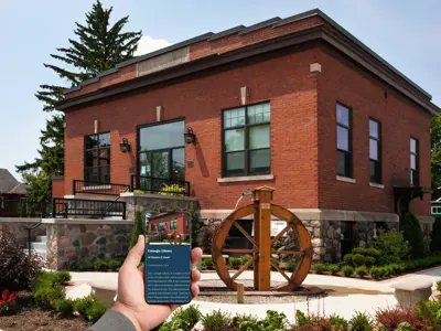 A person standing in front of a building holds out a smartphone displaying a photo and details about that same building