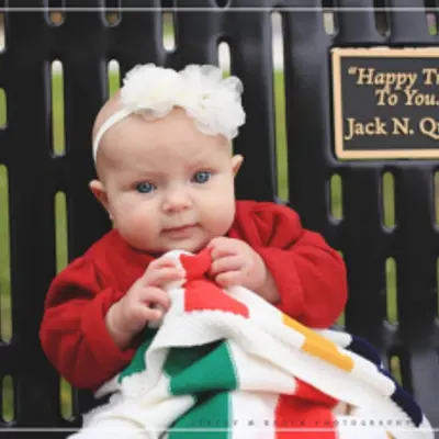 Baby sits on bench with plaque tribute that reads: "Happy Trails to You - Jack N. Queen"