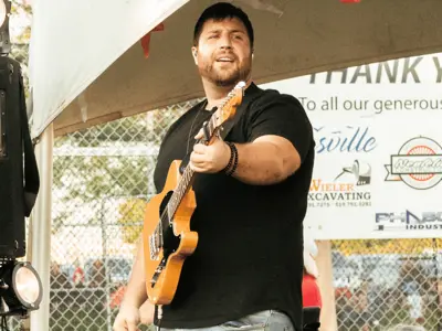 Musician performs on stage, with a sponsorship billboard behind him