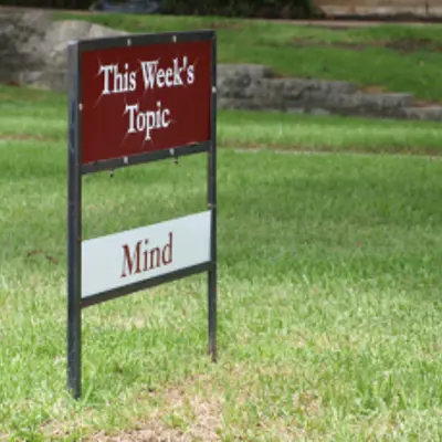 A portable sign stuck in grass reads "This Week's Topic, Mind"