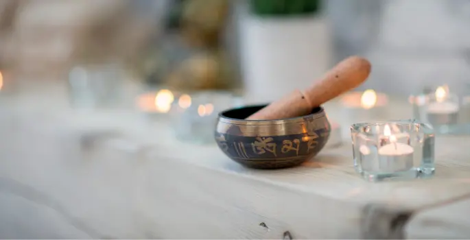 Singing bowl sits on table covered with tealights