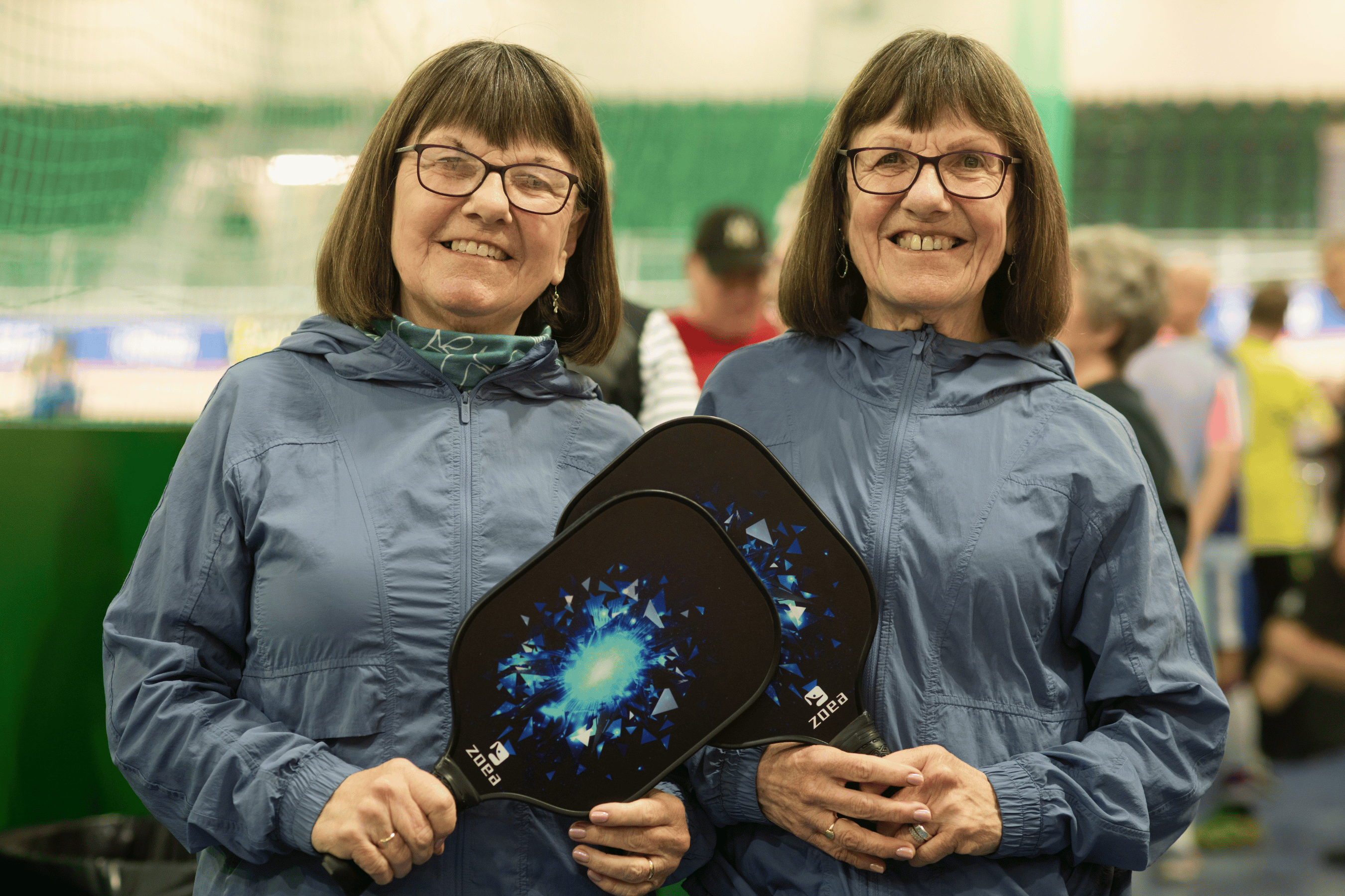 Twin women smile with matching pickleball paddles