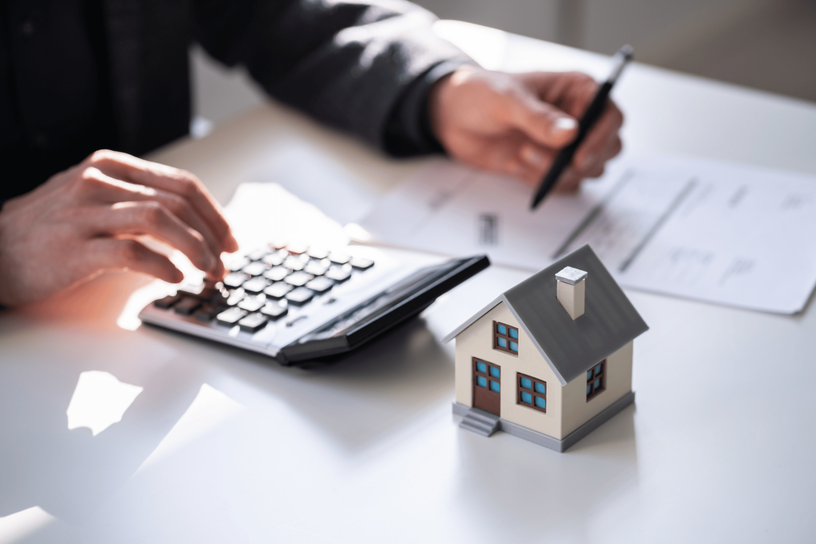 model home on table while a man uses a calculator to fill out a form.
