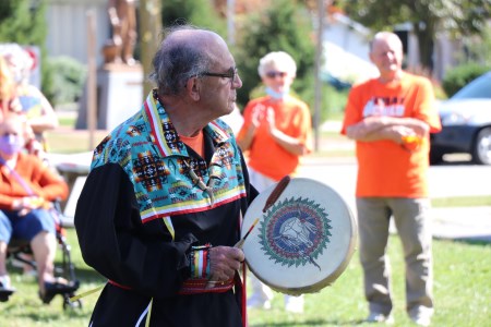 A local Indigenous community member performs a ceremonial drumming in front of a crowd