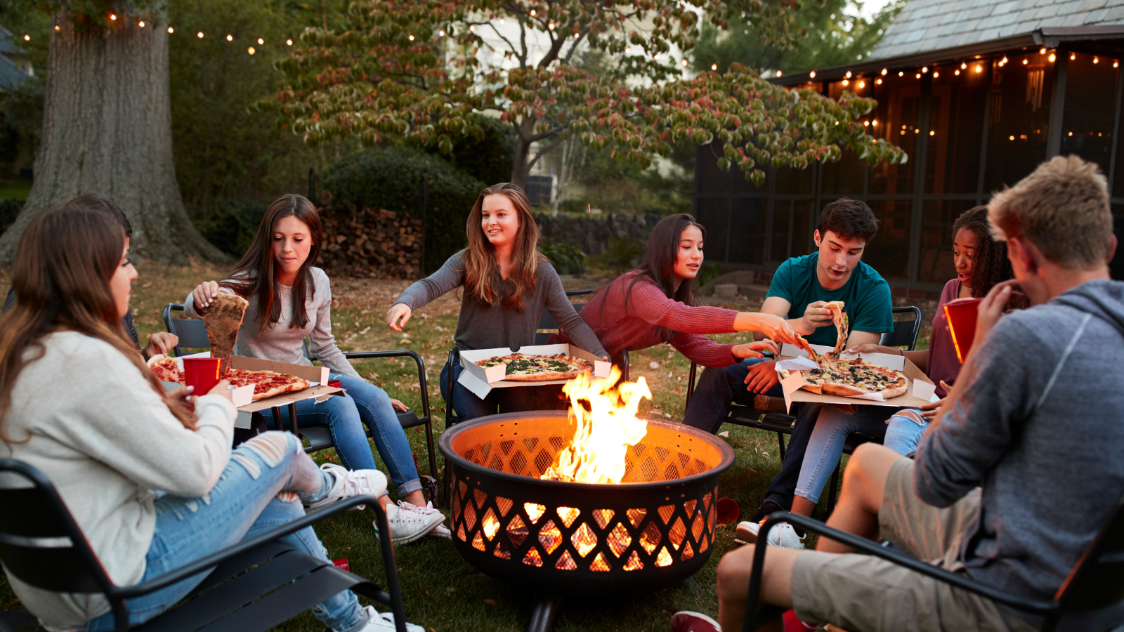 A group of young people sit around an open fire eating pizzas