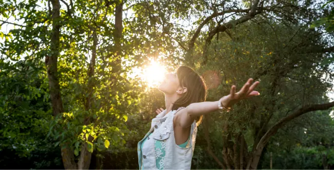 Woman reaches out to the sky in a park-like setting