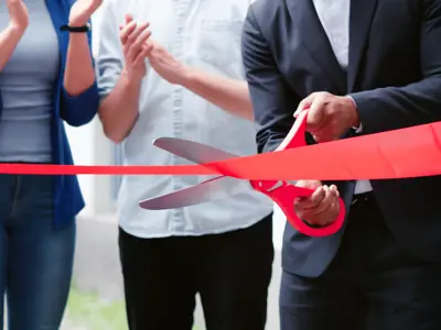 Large scissors cut red ribbon signifying the opening of a new business