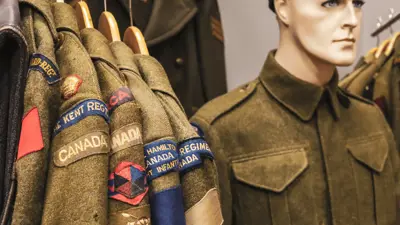 Multiple uniforms hang beside a mannequin modelling a military uniform