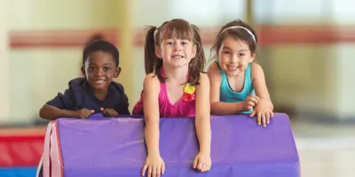 Three smiling kids lean over a gym mat
